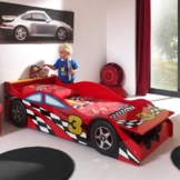 Rotes Kleinkindbett in Rennwagenoptik mit kleinem Jungen der davor spielt